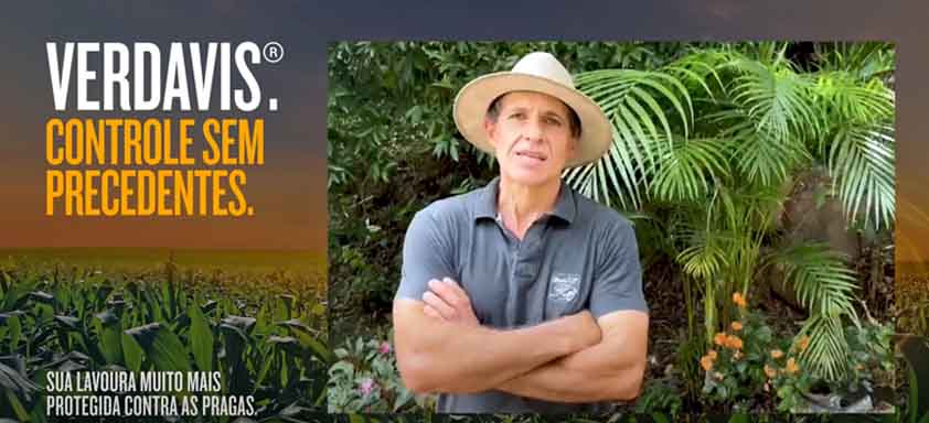 Vilson Signori aparece de braços cruzados em frente a uma plantação de milho, com o letreiro "Verdavis. Controle sem precedentes. Sua lavoura muito mais protegida contra as pragas."